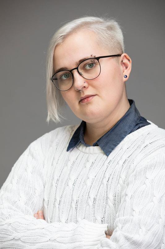 Headshot of Emory, a young White person with bleached grey hair and piercings, wearing glasses.